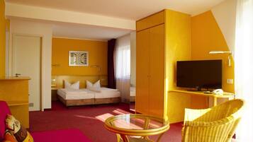 A hotel room with a bed, a television, a small table, and a wicker chair.