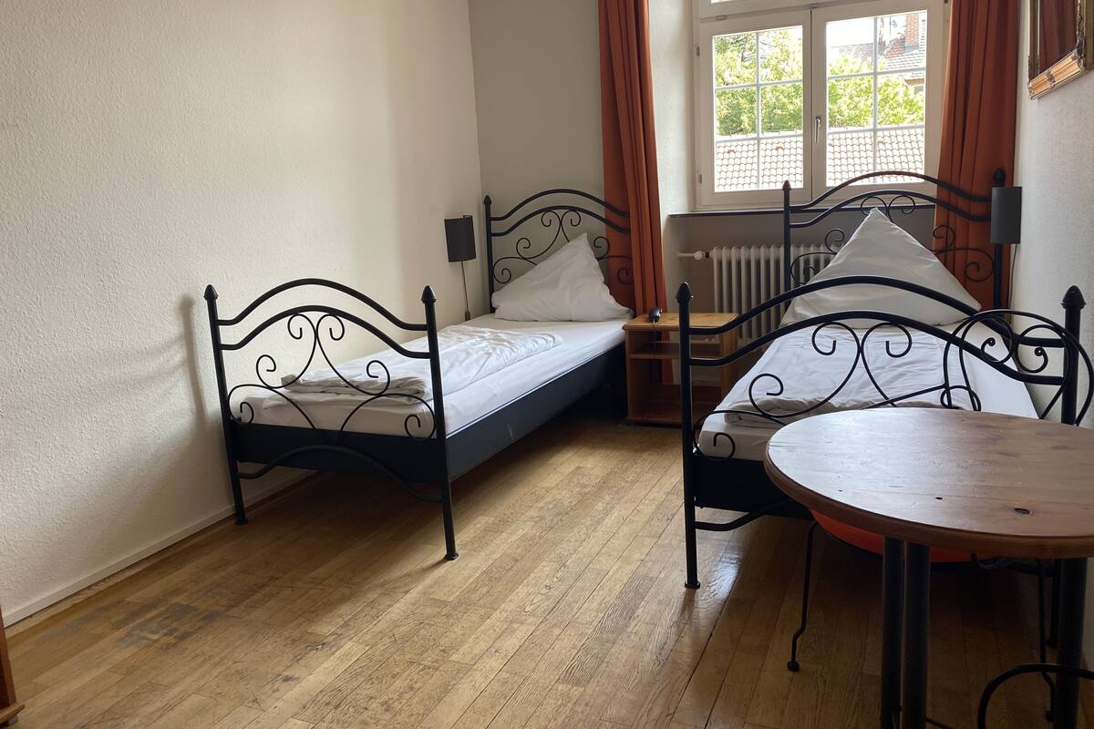 A room with two single beds, a wooden table, and a radiator.