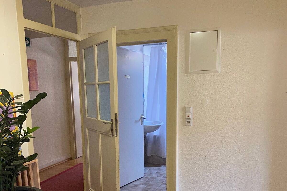 A room with a wooden floor, a white door leading to a bathroom, a potted plant, and a round table.