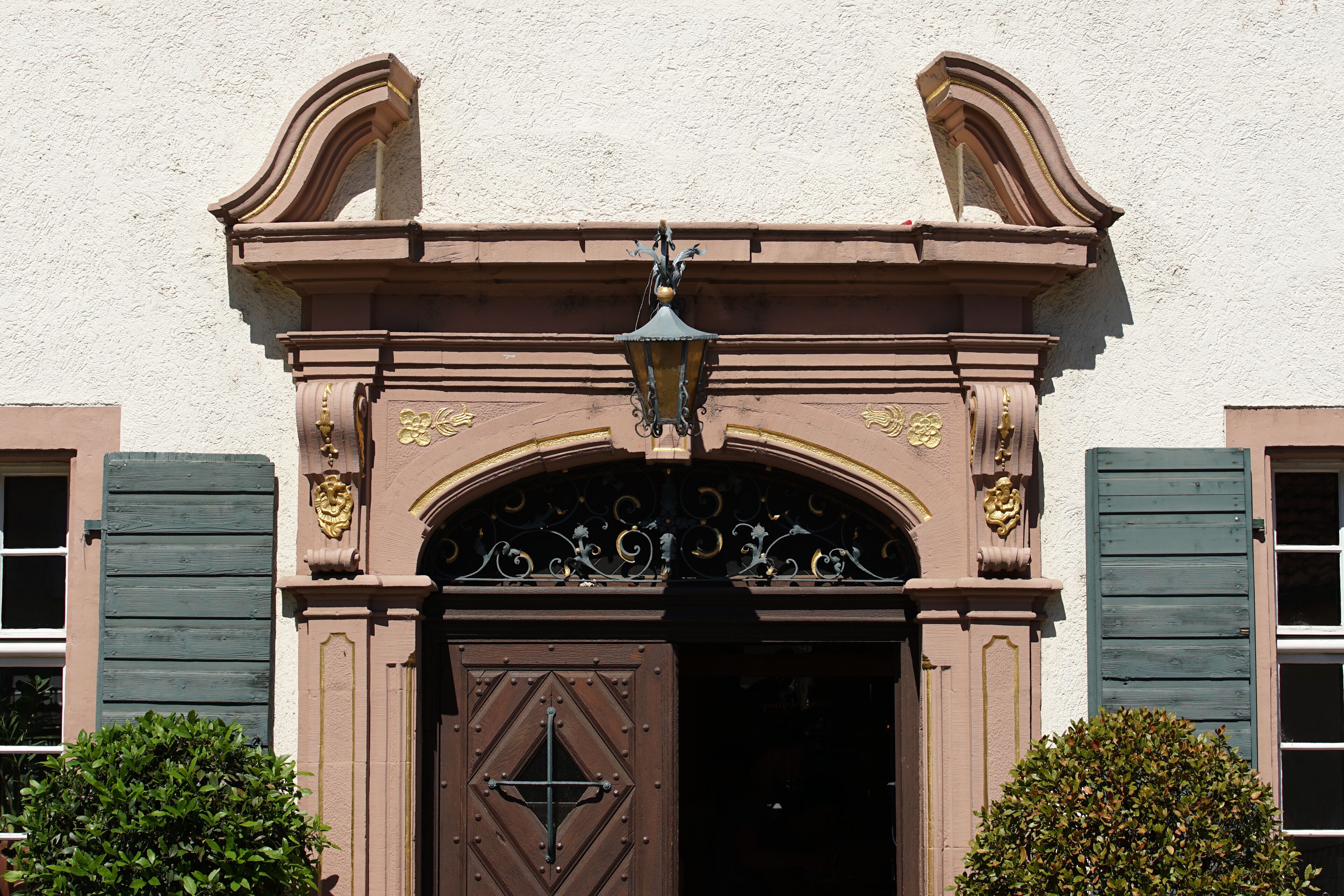 Una entrada de edificio con un arco decorativo, una puerta de madera grande y un farol colgante.