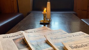 A wooden table with newspapers, a candle, and a vase with flowers. - Hotel Gasthaus Schützen (Freiburg im Breisgau)