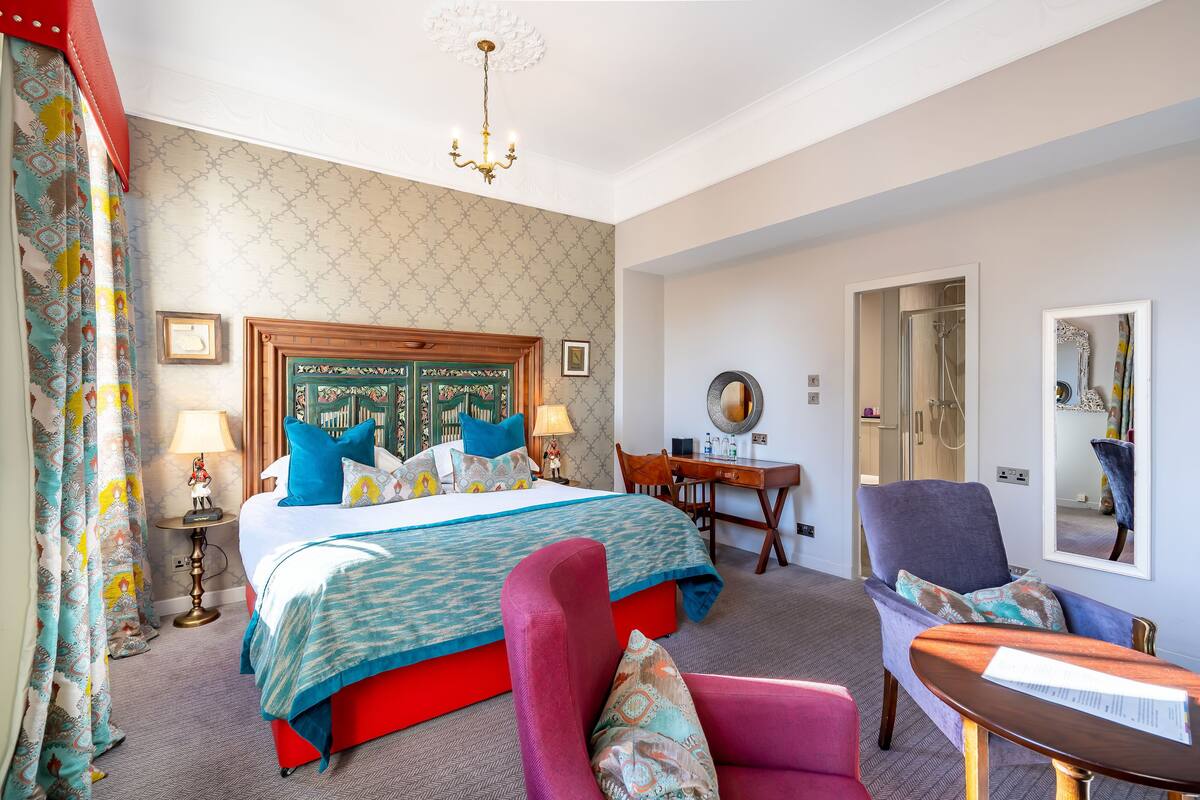 A hotel room with a large bed, a desk, a chair, and a shower area.