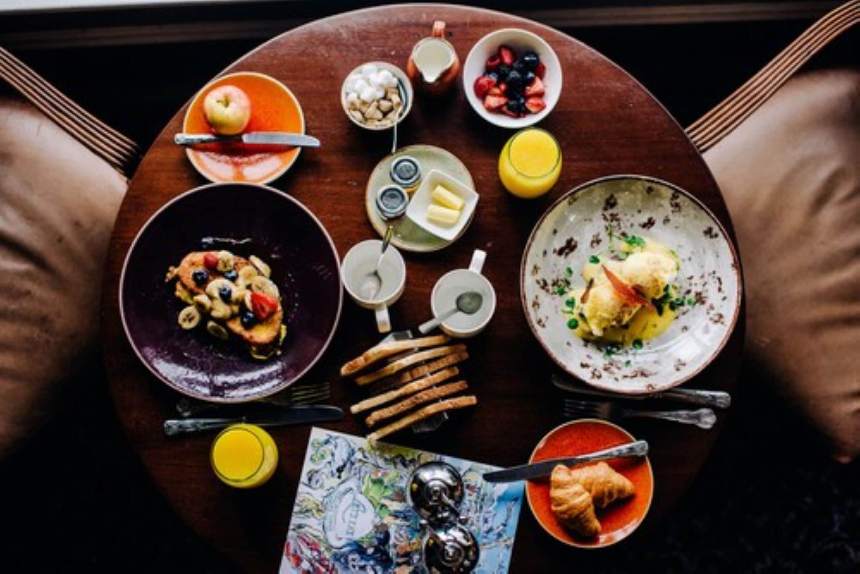 Una mesa con diferentes alimentos para el desayuno, como tostadas, fruta y un tazón de sopa.