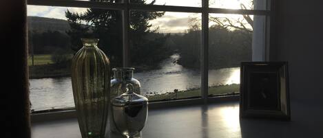 Una ventana con vista a un río y árboles, un florero y un pequeño cuadro en un adorno de mesa.