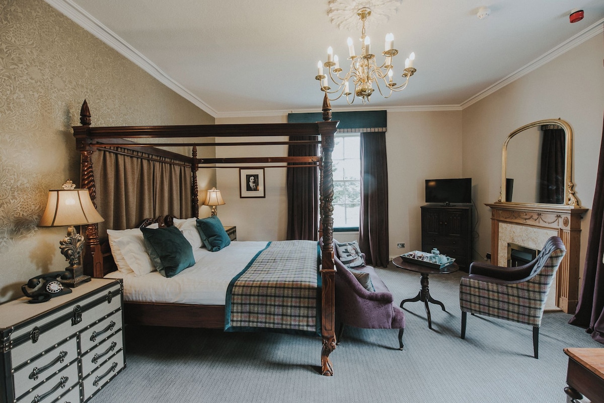 A four-poster bed with a chandelier, a television, a fireplace, and a chair in a hotel room.
