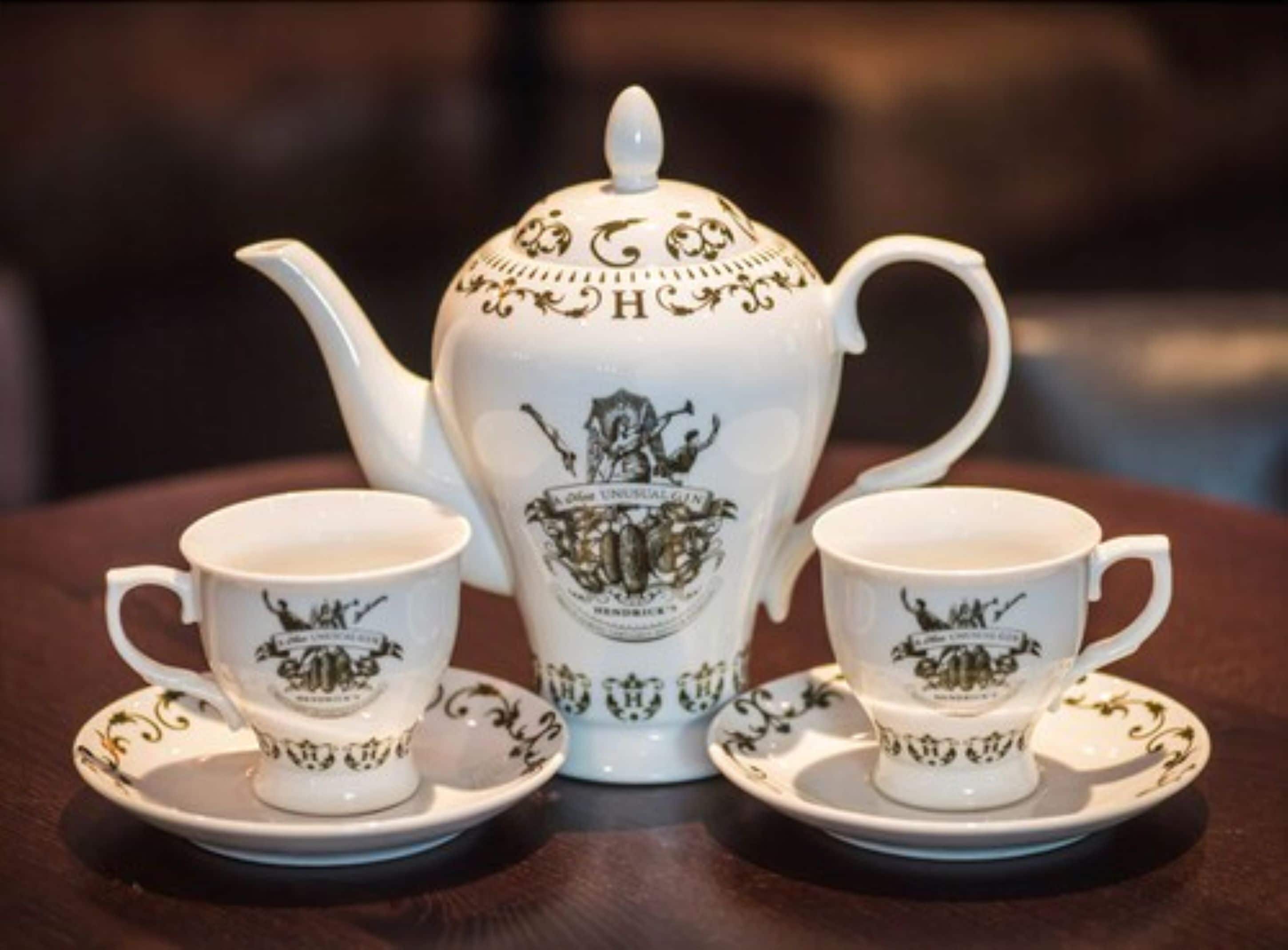 A tea set with a teapot and two cups, each with matching saucers, on a wooden table.