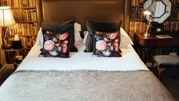 A neatly made bed with floral pillows, a bedside table with a lamp, and a bookshelf in the background.