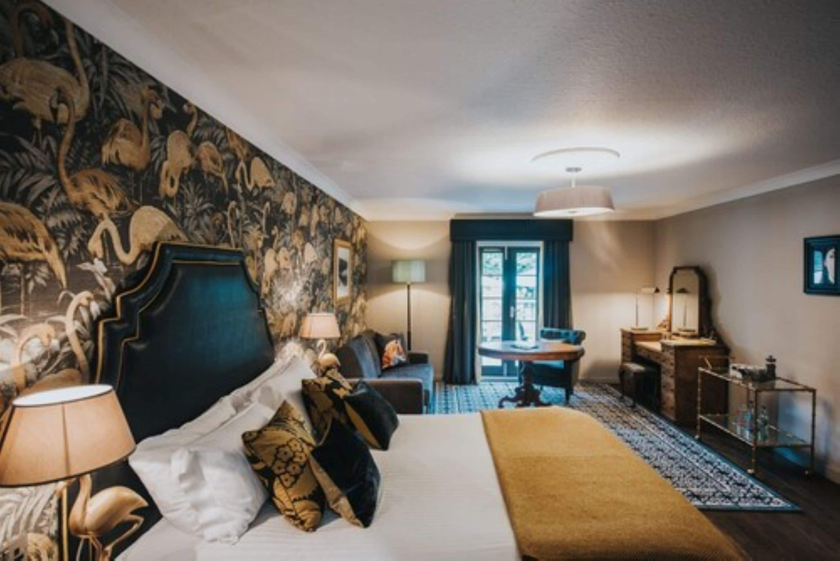 A hotel room with a large bed, a desk, a chair, a lamp, and a window.