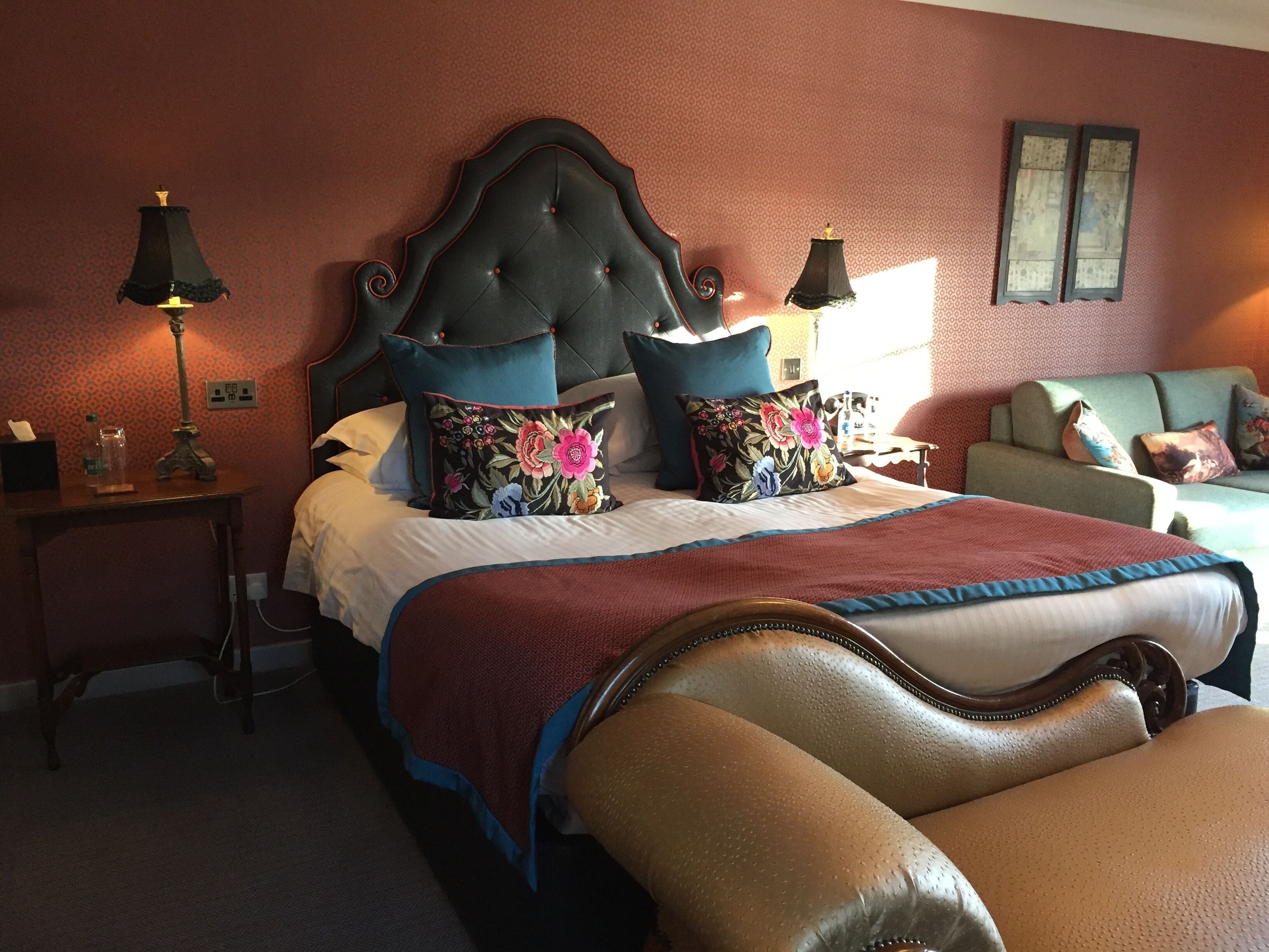 Habitación de hotel con una cama grande, una mesita de noche con lámpara, un sofá y una silla.