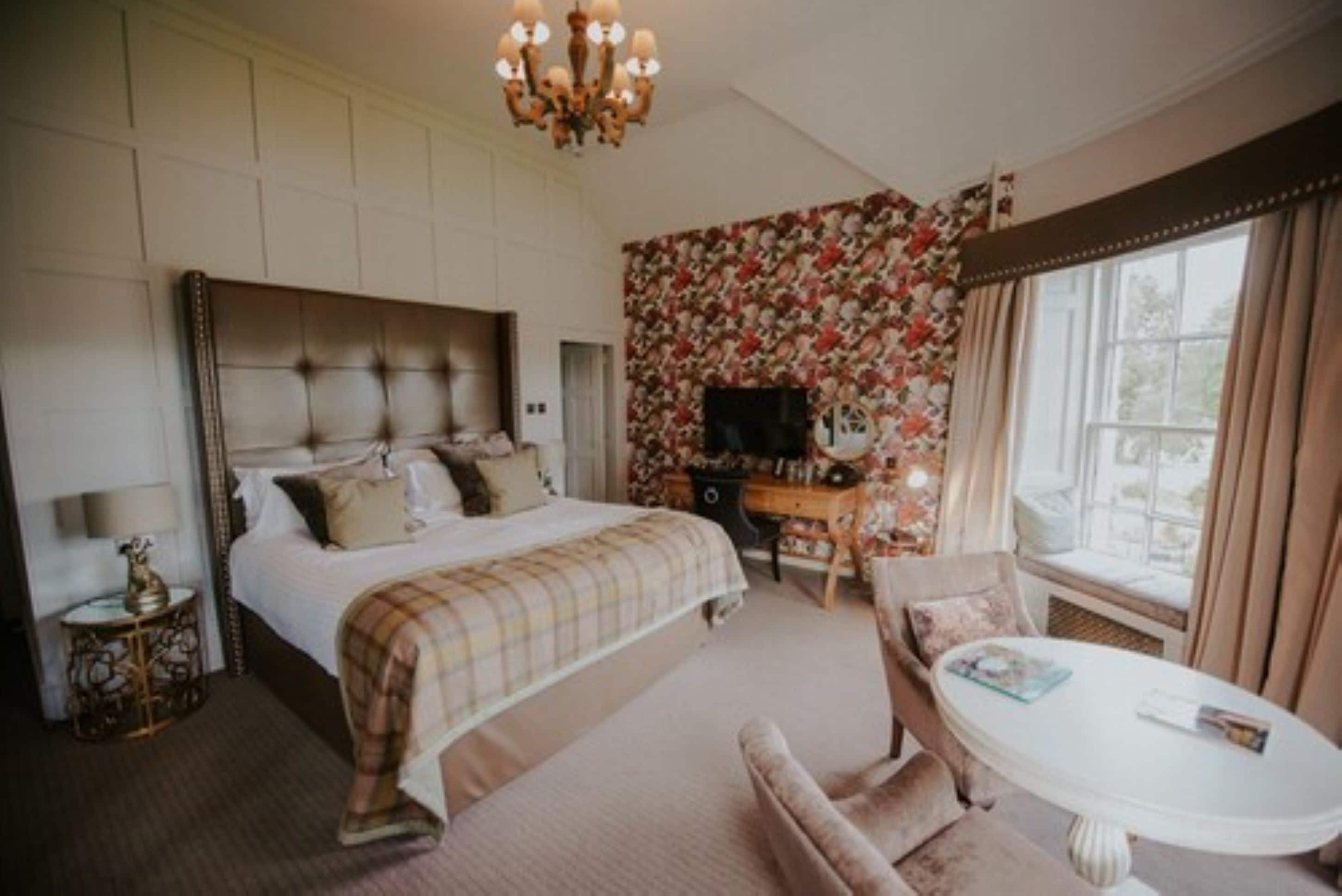 A bedroom with a large bed, a desk, a chair, and a window with curtains.