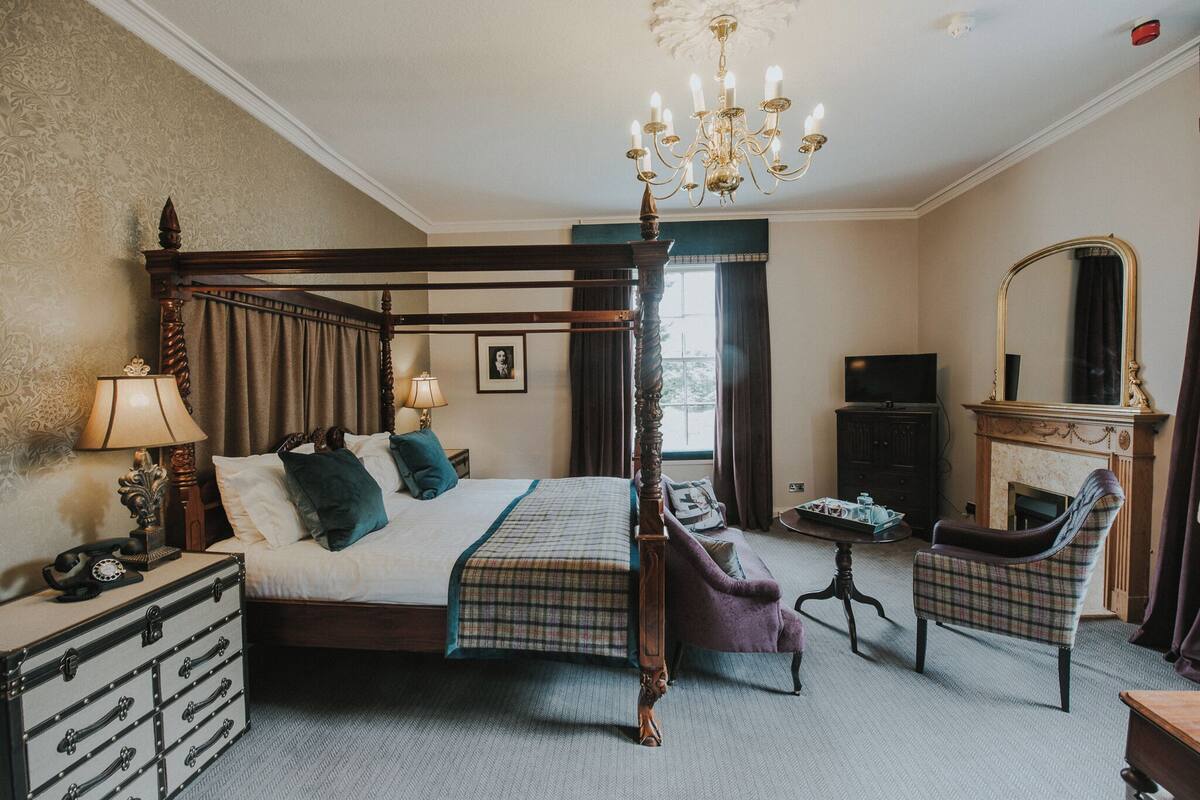 A four-poster bed with a chandelier, a television, a fireplace, and a chair in a hotel room.