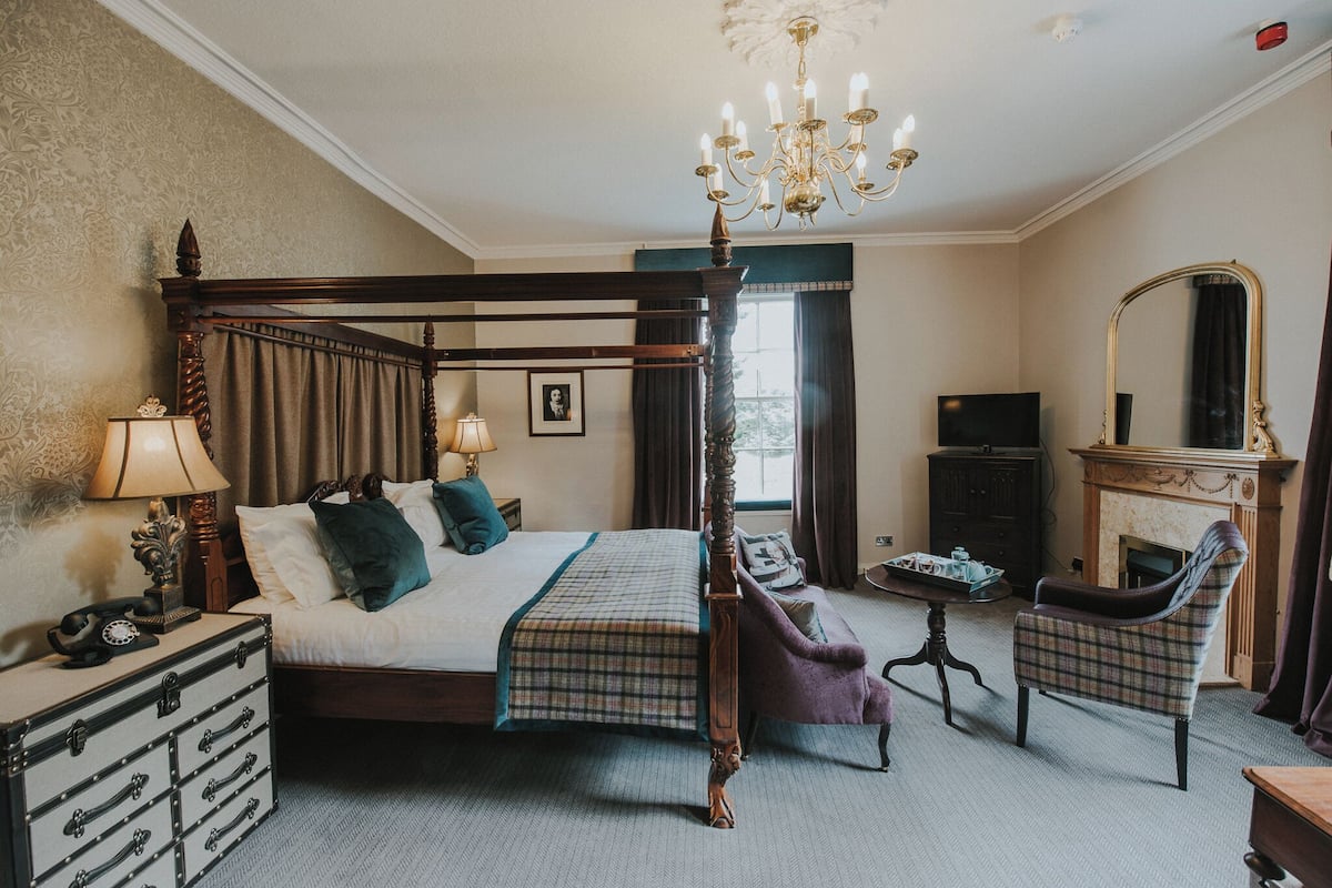 Una cama con dosel, lámpara de araña, televisor, chimenea y una silla en una habitación de hotel.