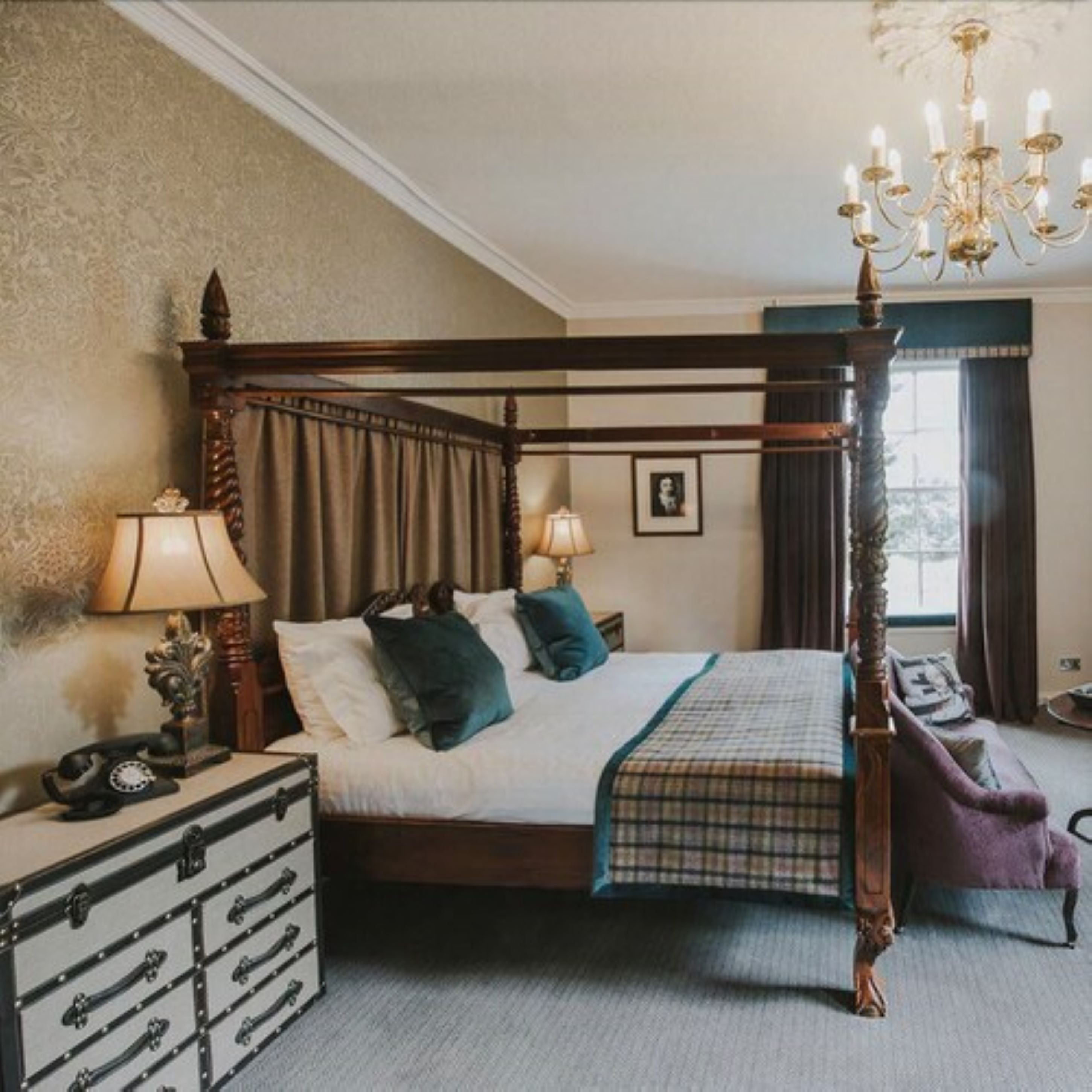 A four-poster bed with a wooden frame, a bedside table with a lamp, and a dresser with multiple drawers.