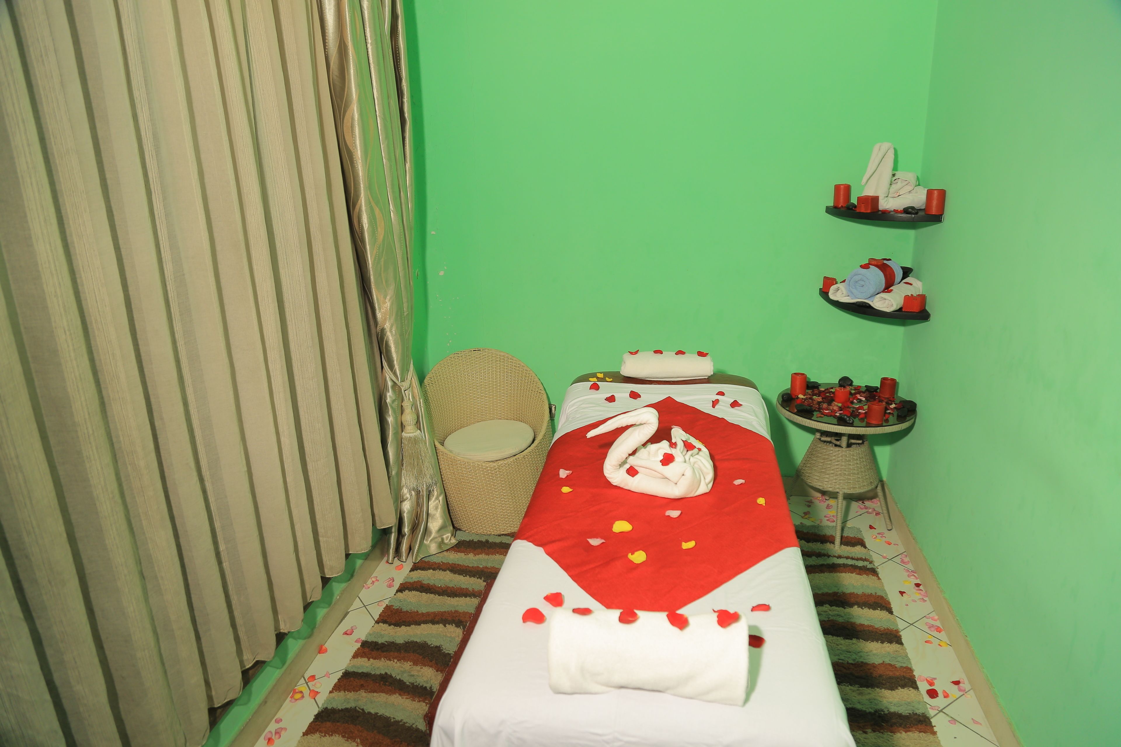 A room with a bed, a wicker chair, a small table with candles, and a shelf with towels.
