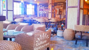 Un interior de restaurante con muebles de mimbre, piso de baldosas y varios objetos decorativos en las paredes.