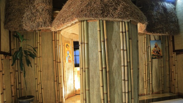 Una estructura tradicional de bambú con techo de paja, una planta en maceta y un cuadro en la pared.