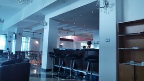 Un amplio hall de hotel con zona de bar, disposición de asientos y una cocina visible al fondo.