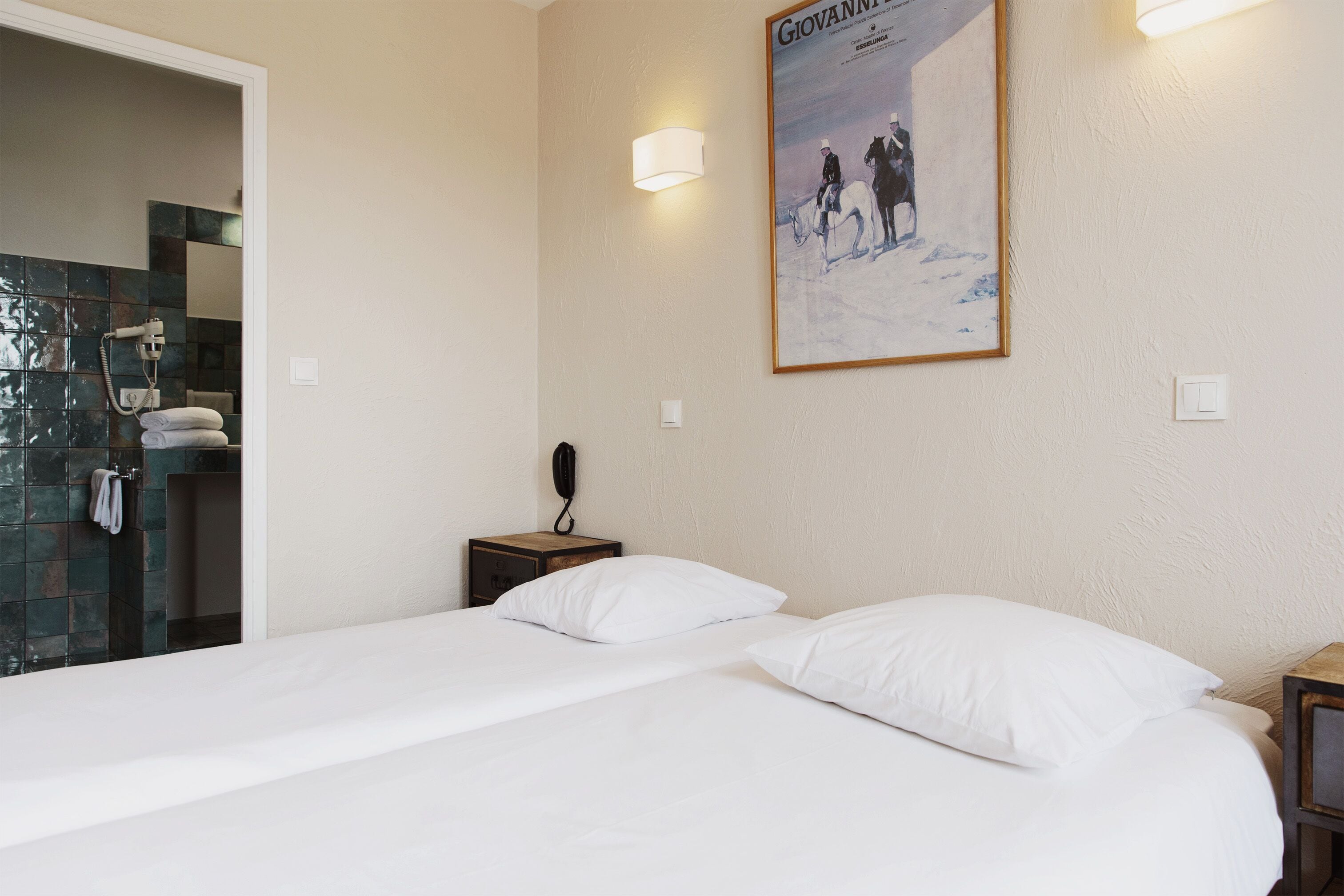 A hotel room with a bed, a nightstand, a telephone, and a poster on the wall.