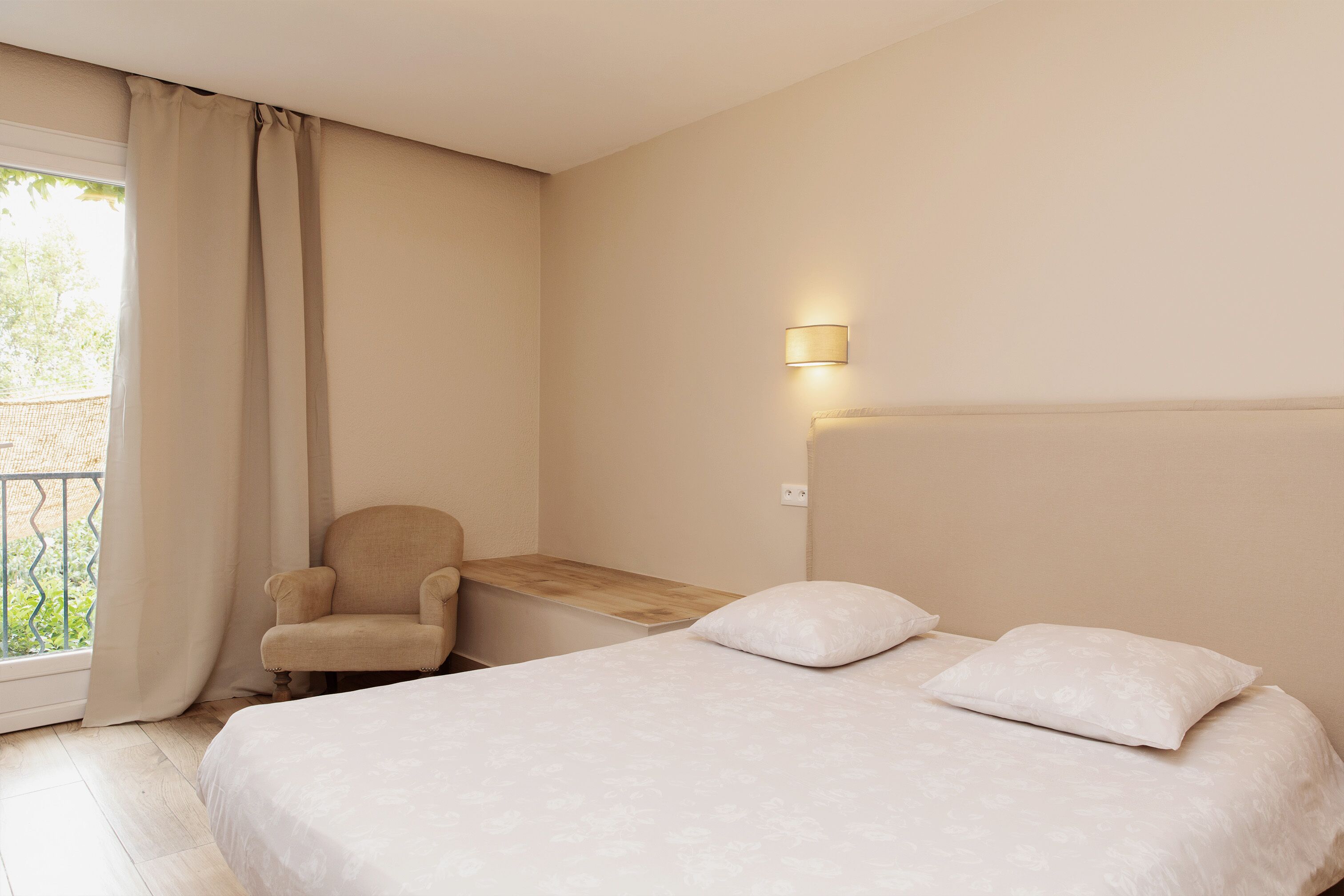 A hotel room with a bed, a chair, a small table, a lamp, and a window with curtains.