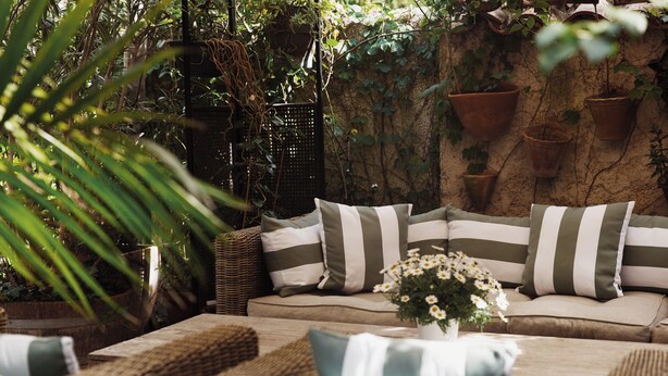 A cozy outdoor seating area with a cushioned sofa, striped pillows, and a small table with a vase of flowers. - Coq Hôtel (Cogolin)