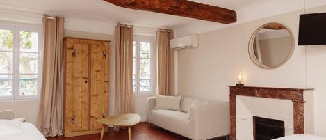 A room with a wooden wardrobe, a white sofa, a small table, a fireplace, and a TV mounted on the wall.