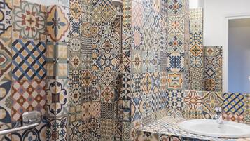 A bathroom with a sink and a shower. The walls are covered with patterned tiles.