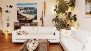 A living room with a white sofa, a coffee table, and a painting of a coastal scene. - Coq Hôtel (Cogolin)