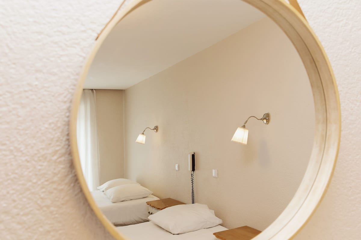 A bedroom with two beds, a bedside table, a lamp, and a wall-mounted phone.