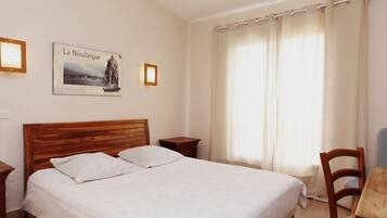 A neatly made bed in a room with a wooden headboard, a small wooden nightstand, a framed picture on the wall, and a window with curtains.