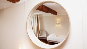 A circular mirror reflecting a room with a bed, a chair, and a wall-mounted light fixture. - Coq Hôtel (Cogolin)