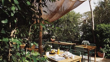 An outdoor dining area with wooden tables and chairs, surrounded by greenery and potted plants.