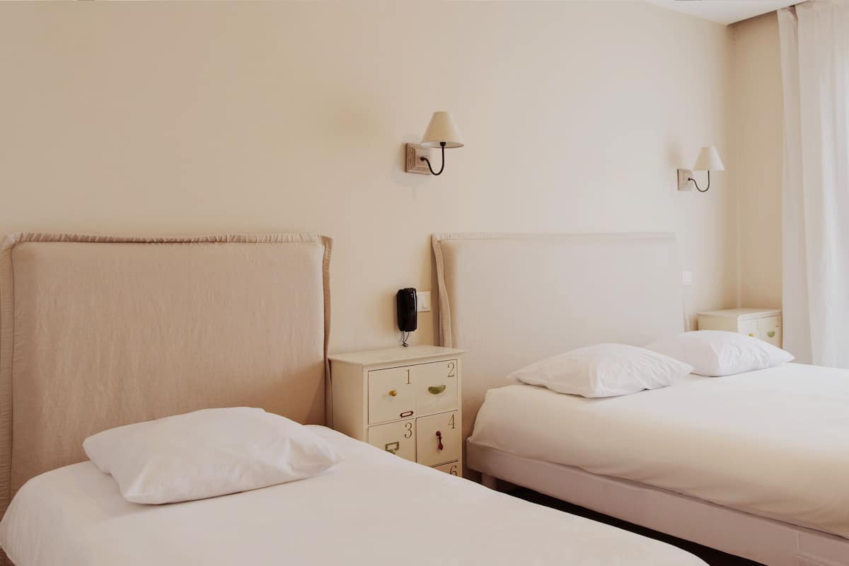 A hotel room with two beds, a bedside table with a lamp, a phone, and a small cabinet.