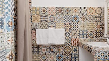Un baño con un muro de azulejos que presenta una variedad de patrones geométricos y florales. Hay una toalla blanca colgada en la pared, un lavamanos y una cortina de ducha.