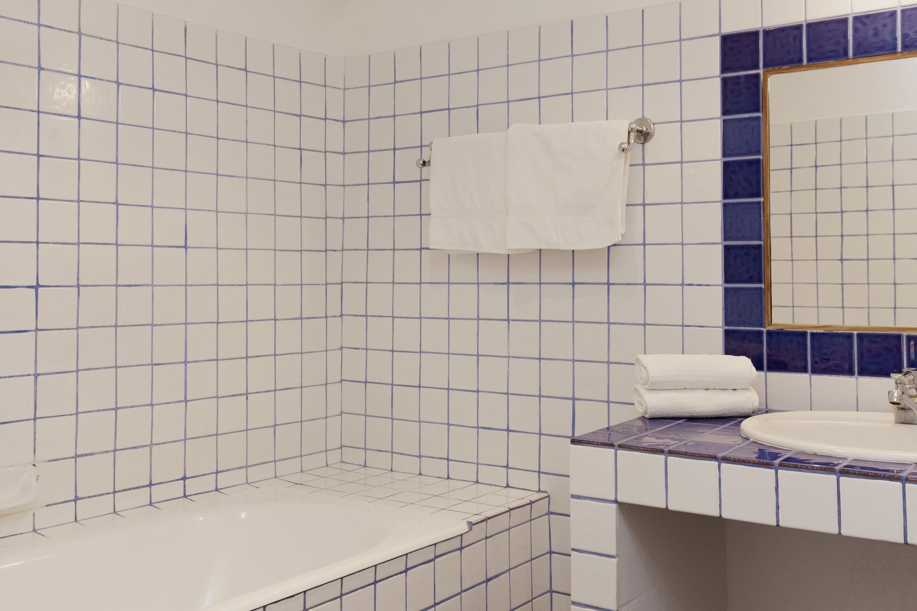 Un baño con azulejos blancos y azules, una bañera blanca y un lavabo con un espejo encima.