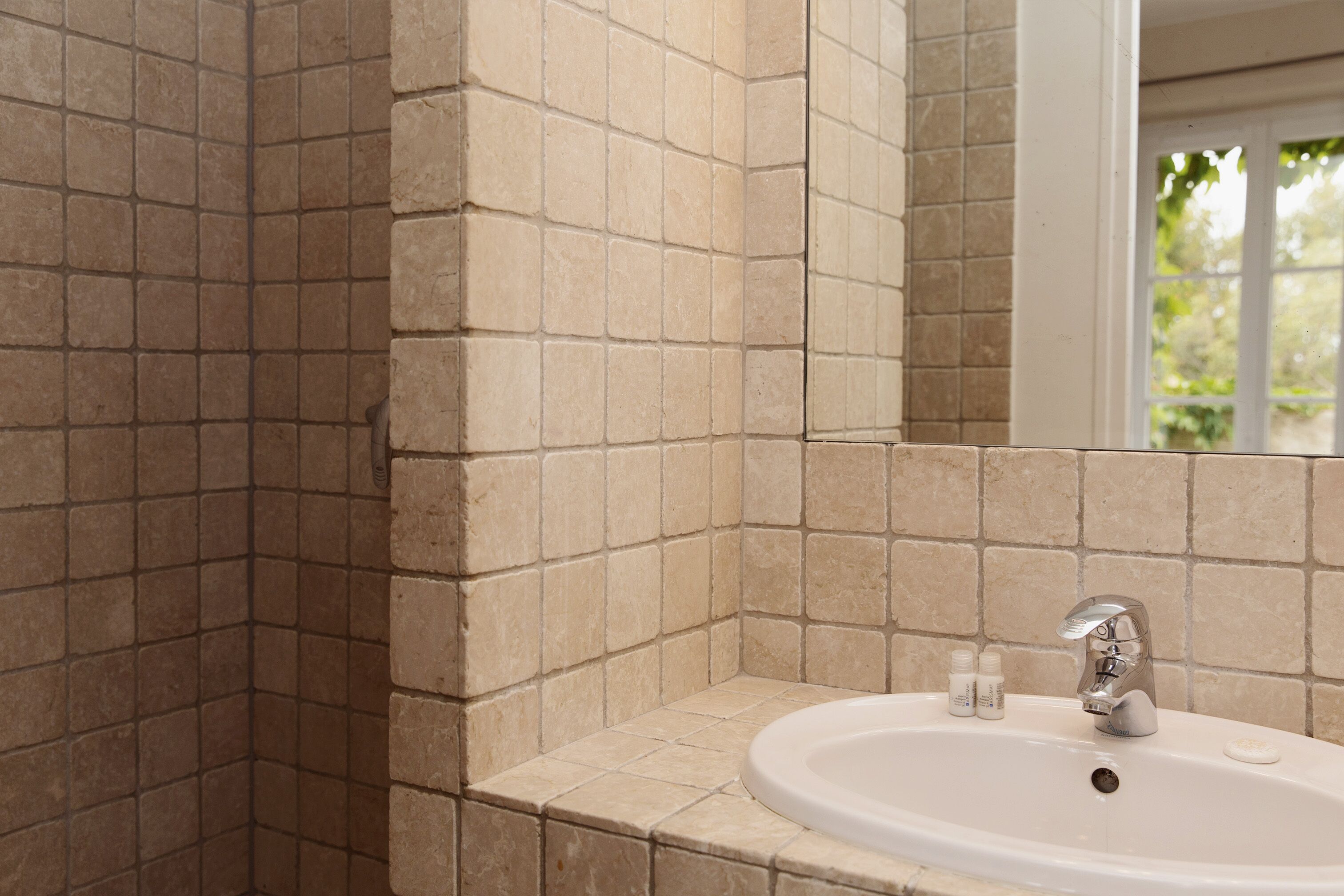 Ein Badezimmer mit beigelfarben gefliesten Wänden und einem weißen Waschbecken mit moderner Armatur.