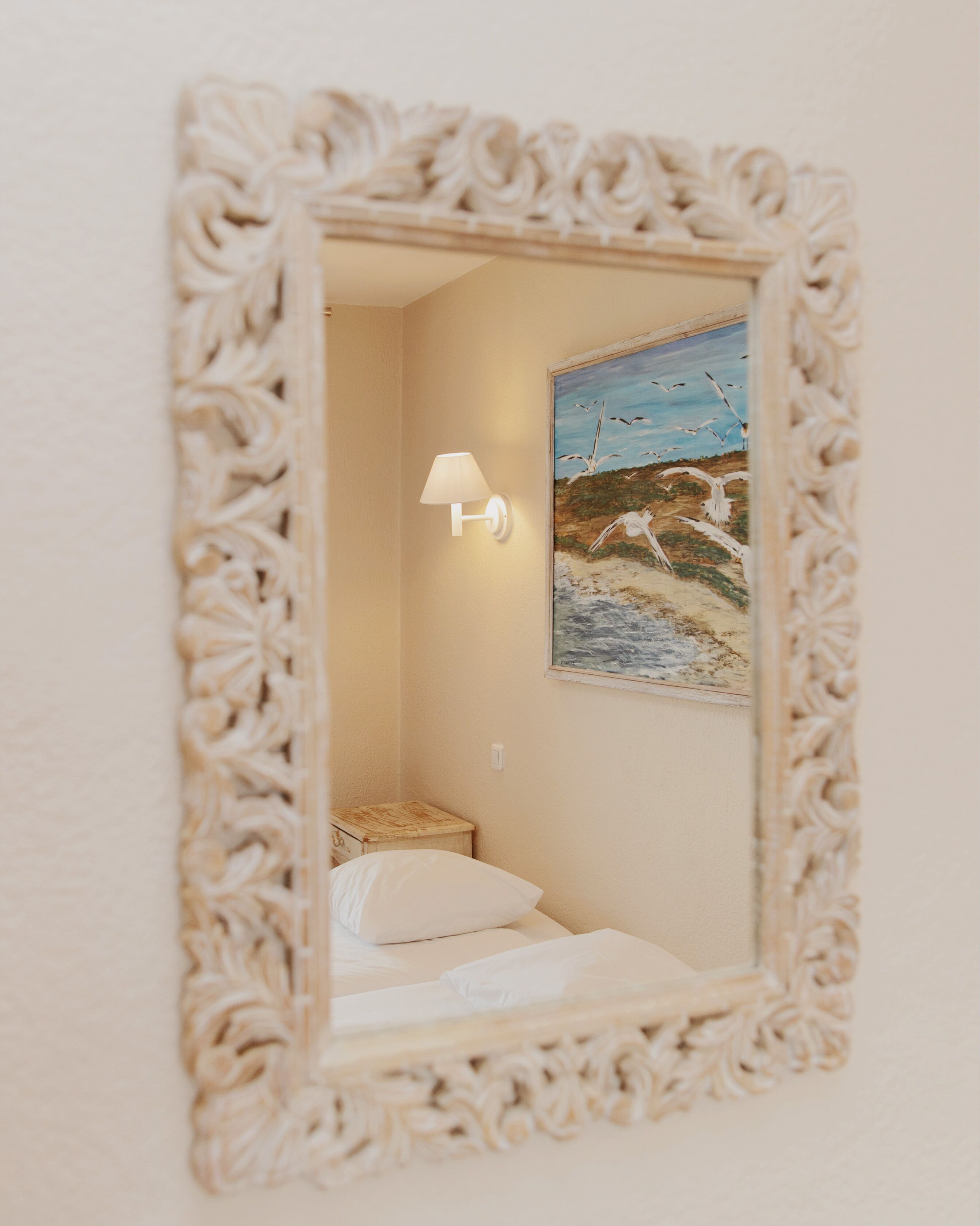 A room with a bed, a wall-mounted lamp, and a painting of birds on the wall.