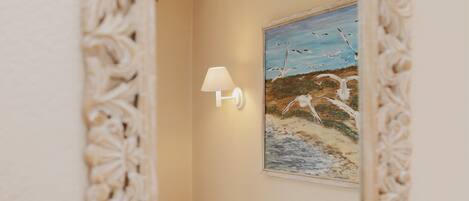 A room with a bed, a wall-mounted lamp, and a painting of birds on the wall.