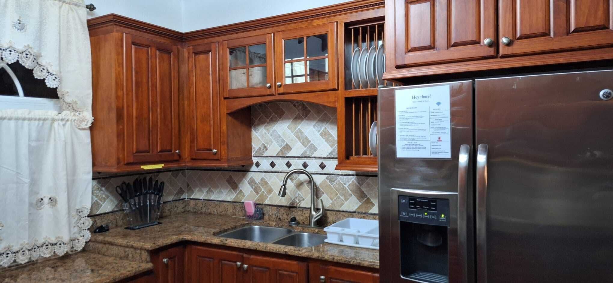 A kitchen with wooden cabinets, a stainless steel refrigerator, a sink, and a tiled backsplash.