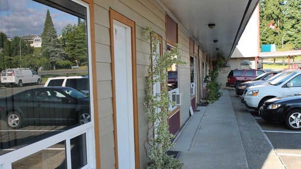 A row of parked cars along a building's exterior. - Redford Motel (Port Alberni)