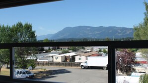 A view through a window of a parking lot with a white truck, a white van, and a building with a satellite dish. - Redford Motel (Port Alberni)