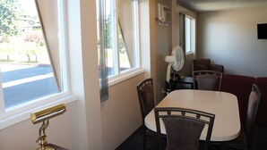 A dining area with a table and chairs, a window with curtains, and a wall-mounted fan. - Redford Motel (Port Alberni)