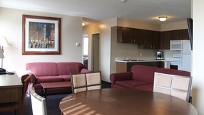 A compact living space with a dining table, two sofas, a kitchen area, and a framed cityscape painting. - Redford Motel (Port Alberni)