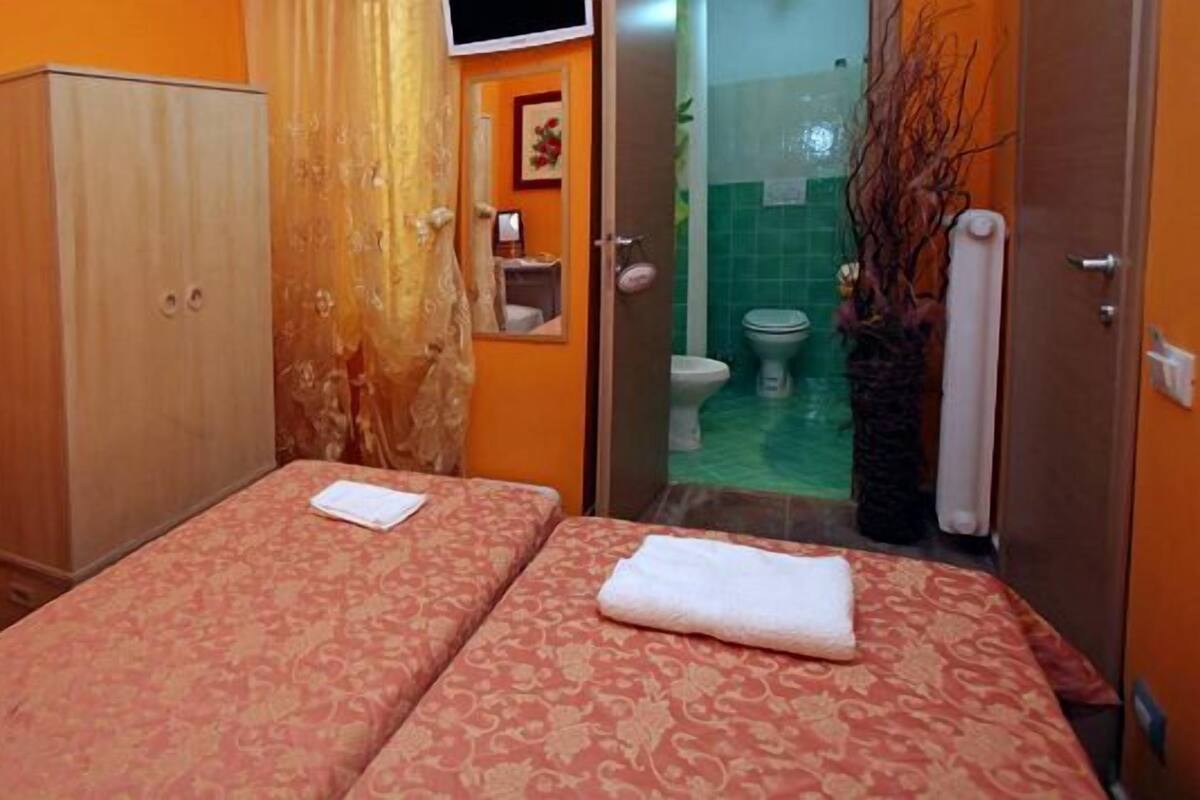 A room with two beds, a wardrobe, a bathroom with a shower, and a toilet.