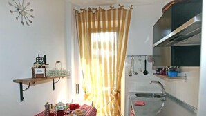 Eine kompakte Küche mit einem kleinen Frühstückstisch, einem hängenden Topfregal und einem Fenster mit Vorhängen.