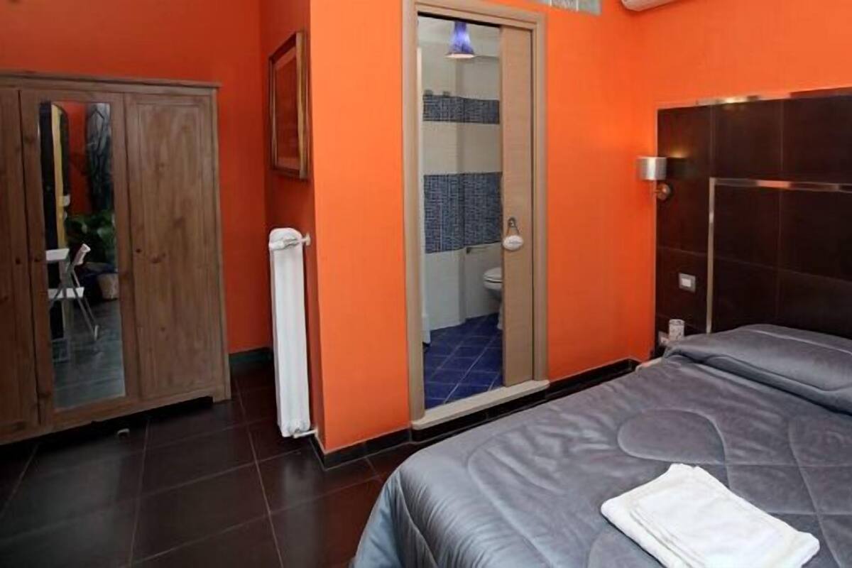 A hotel room with a bed, a wardrobe, and a bathroom visible through an open door.