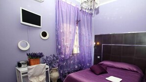 Ein Schlafzimmer mit Bett, Schreibtisch, Stuhl, Fernseher und einem Fenster mit Vorhängen.