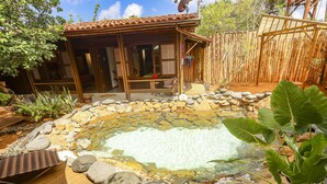 A wooden house with a patio, a hot tub surrounded by rocks, and a bamboo fence. - Beco Pousada Boutique Noronha (Fernando de Noronha)