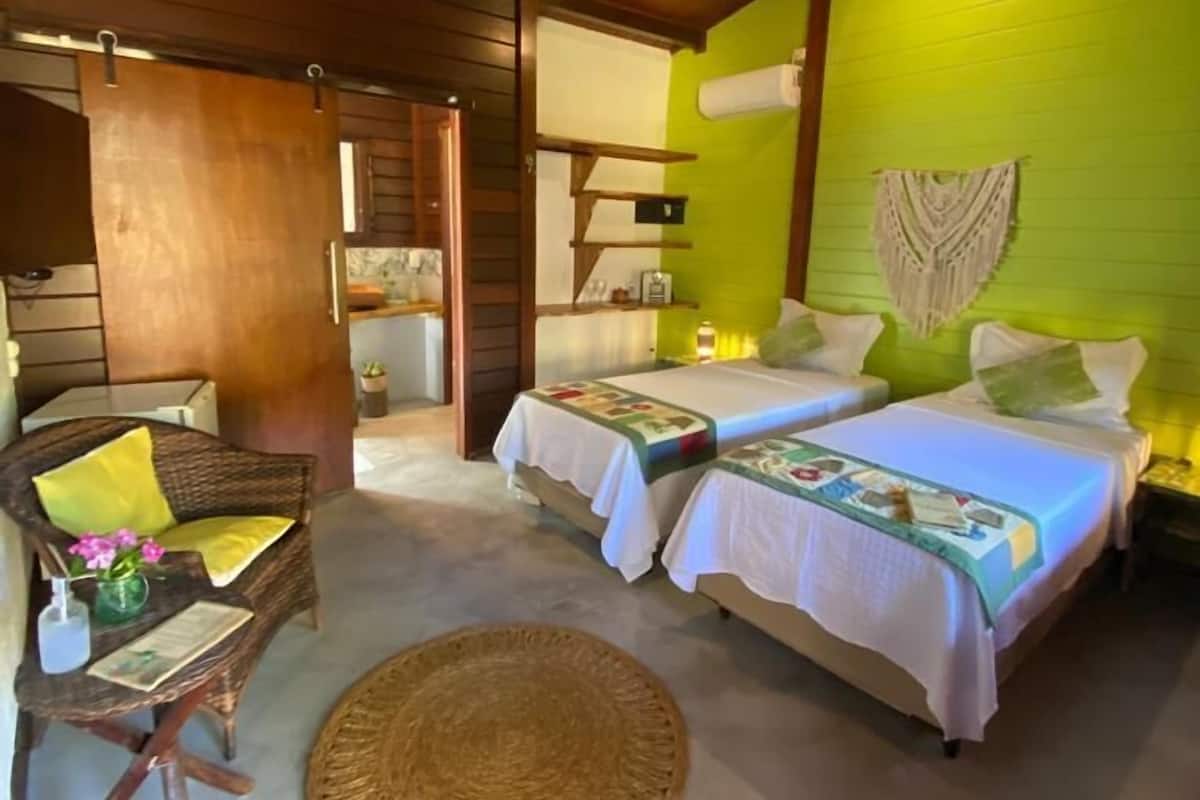 A room with two beds, a ceiling fan, a wicker chair, and a woven mat on the floor.