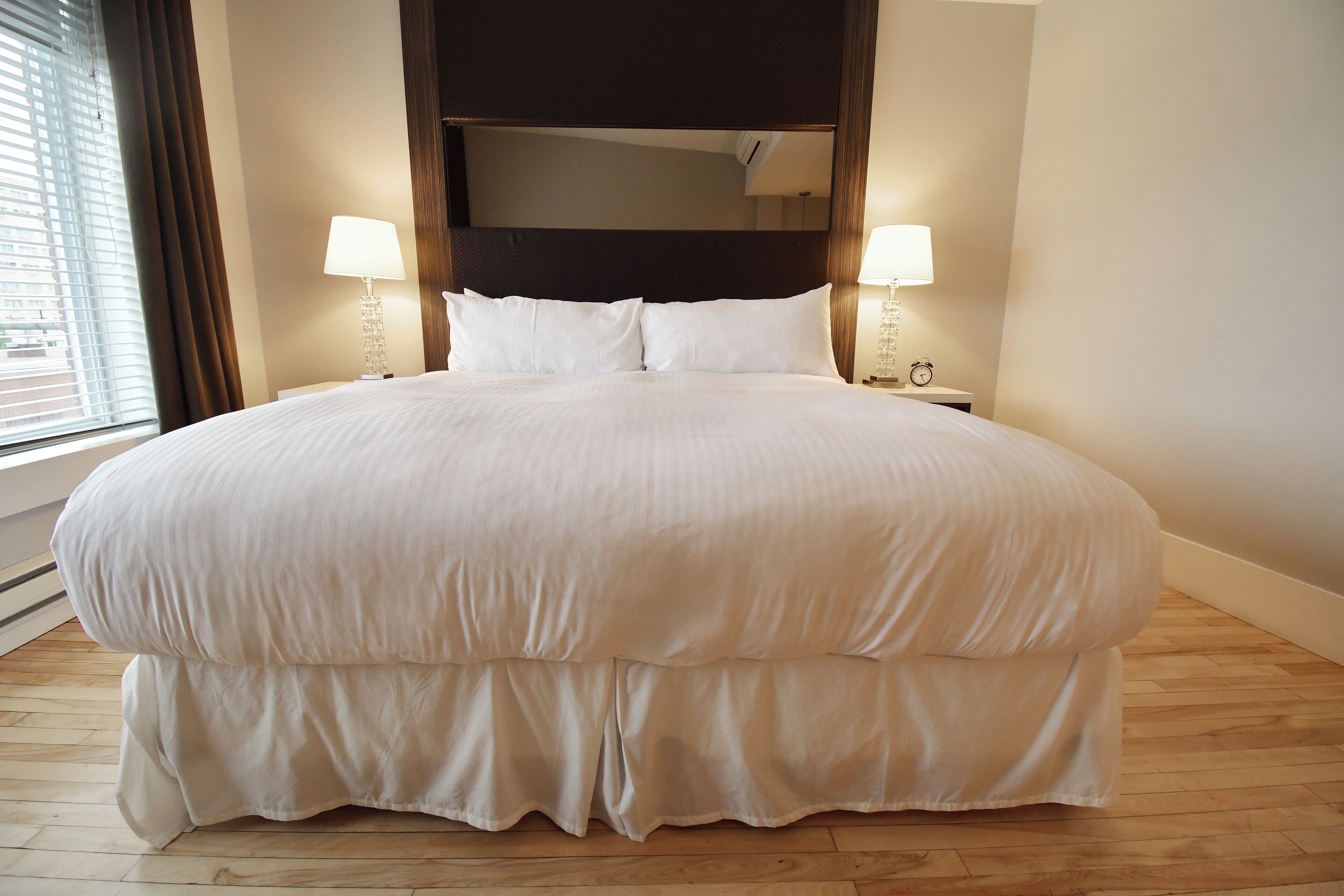 A large, neatly made bed with white bedding, two bedside lamps, and a large mirror above the bed.