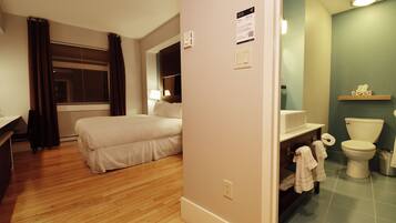 A hotel room with a bed, a bathroom with a toilet and sink, and a wooden floor.